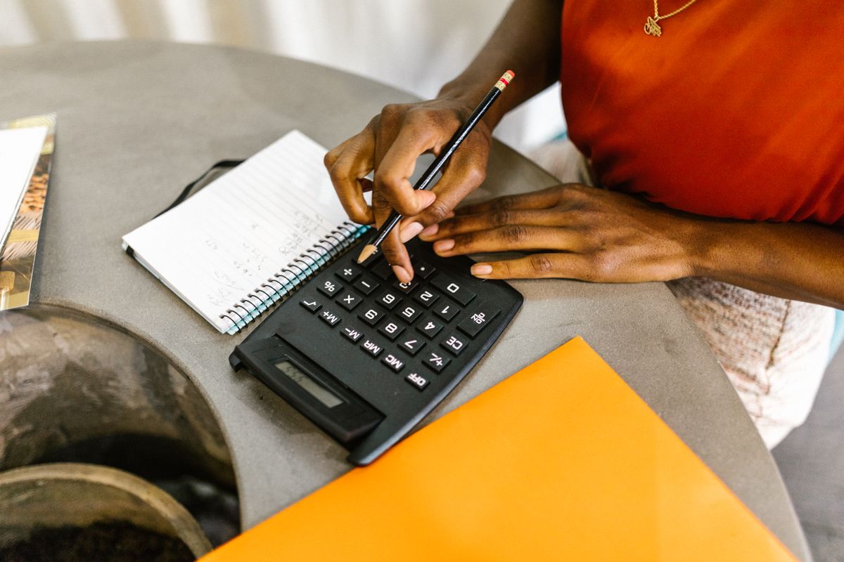 Pessoa usando calculadora e anotações para organizar as contas da casa, com papéis e caneta à mesa.